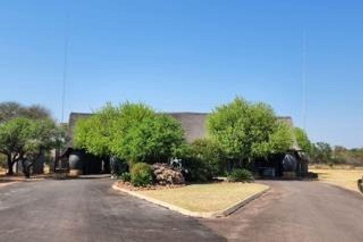 Front view of a property featuring a thatched roof structure, a paved circular driveway, and established garden landscaping.