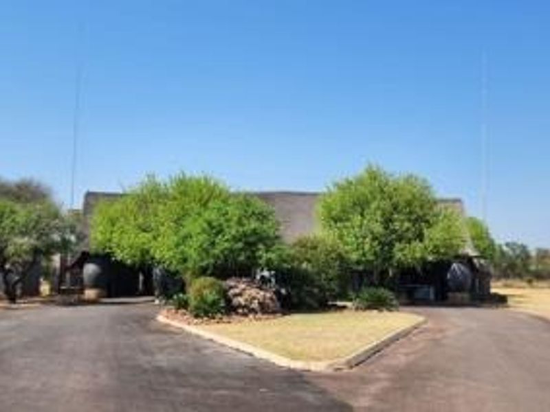 Front view of a property featuring a thatched roof structure, a paved circular driveway, and established garden landscaping.