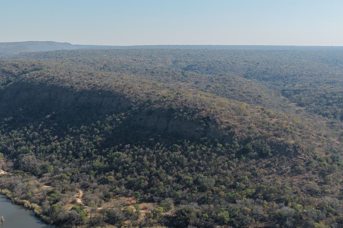 An aerial view of the expansive natural landscape, featuring dense woodland, rugged terrain, and a river flowing through the property.