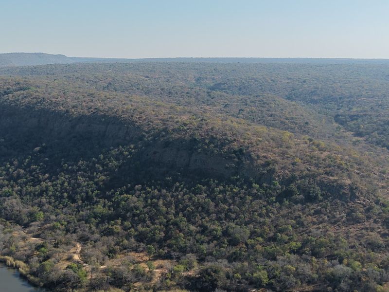 An aerial view of the expansive natural landscape, featuring dense woodland, rugged terrain, and a river flowing through the property.