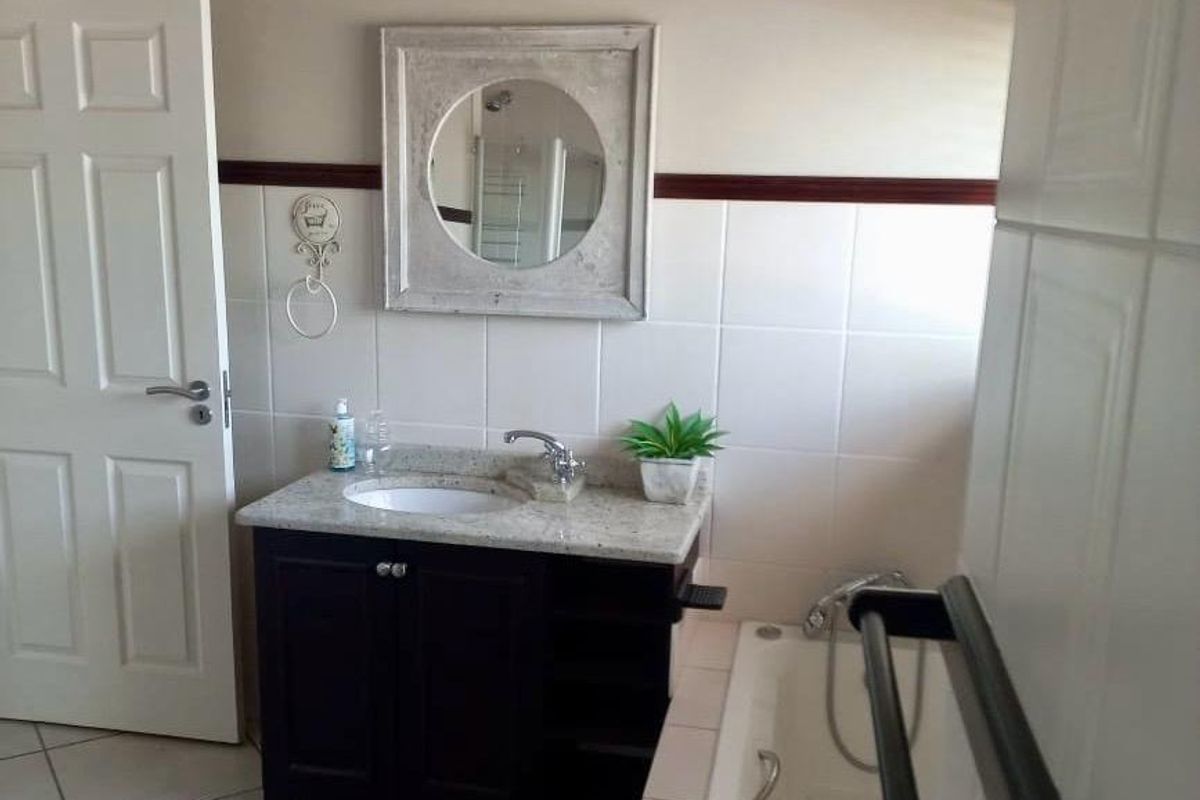 A functional bathroom featuring a dark vanity cabinet with granite countertop, built-in bathtub, and neutral wall tiling.