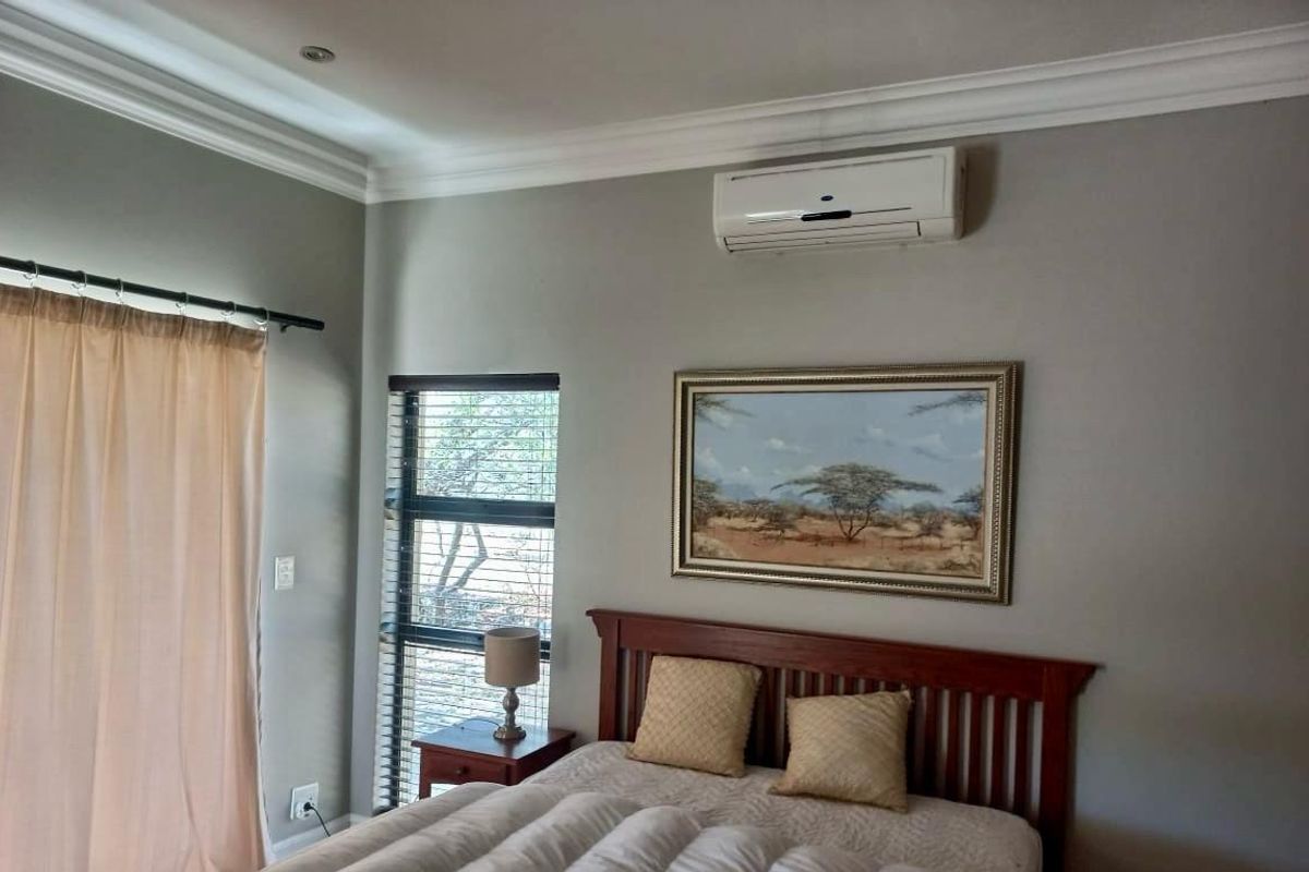 A well-maintained bedroom featuring neutral wall tones, crown molding, a wall-mounted air conditioning unit, and large windows with fitted blinds.