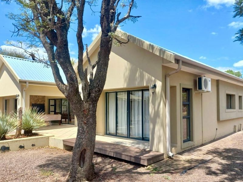 Rear view of the house featuring a metal roof, sliding glass doors, a small deck, and paved pathways in a landscaped garden setting.