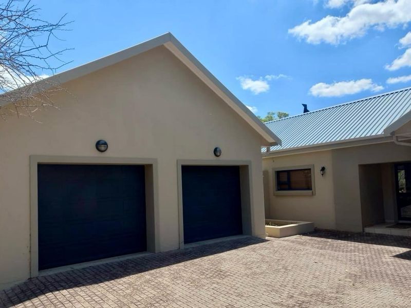 A well-maintained front exterior view featuring a double garage with dark doors, a paved driveway, and a clean metal roof.