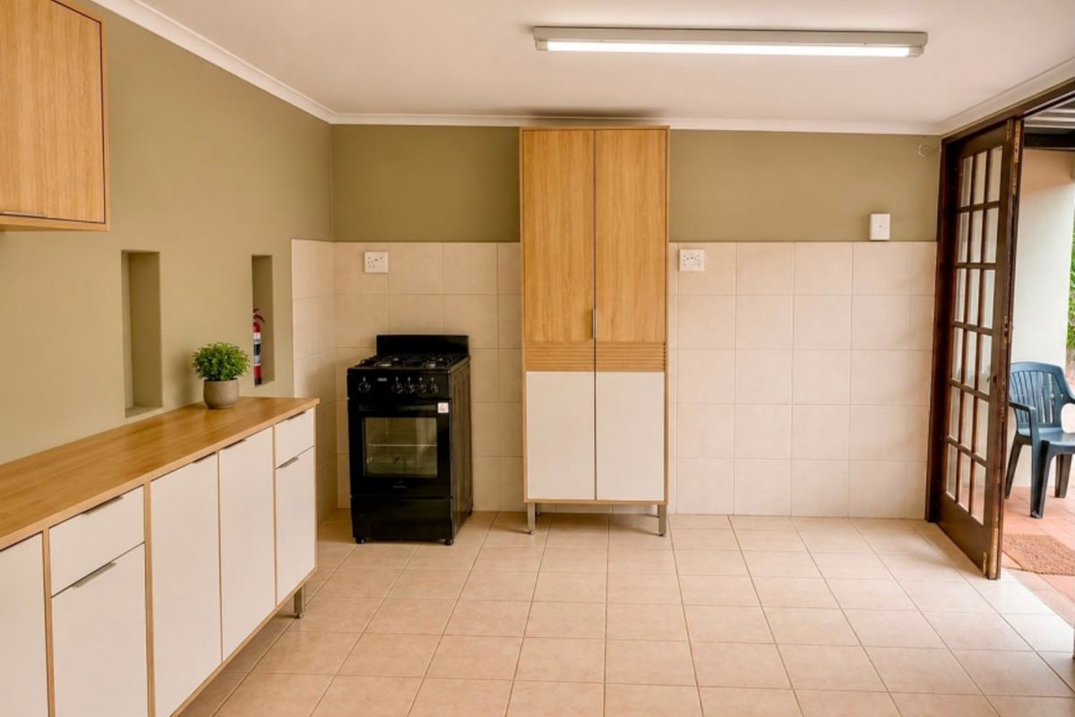 A clean, functional kitchen area featuring tiled flooring, built-in cabinetry, a freestanding stove, and direct access to an outdoor patio through a glass door.