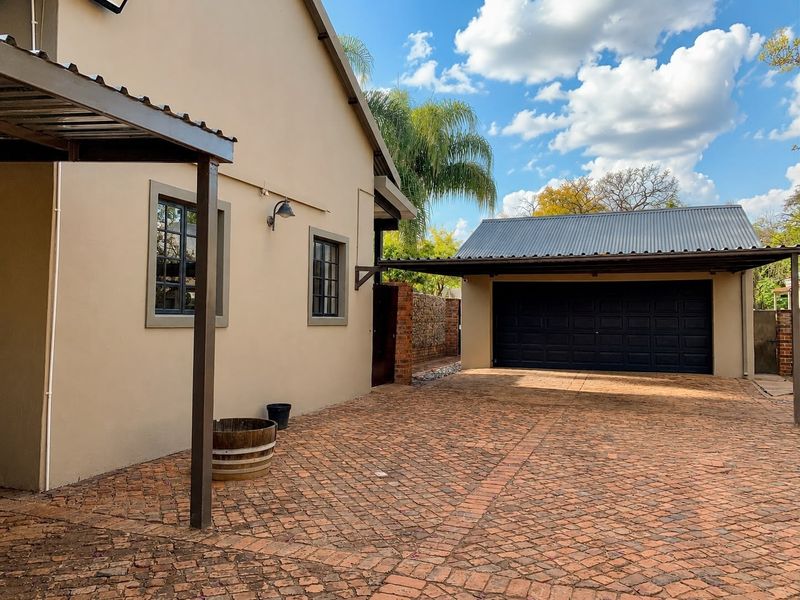 A well-maintained exterior view featuring a brick-paved driveway, a covered carport, and a double garage with a dark sectional door.