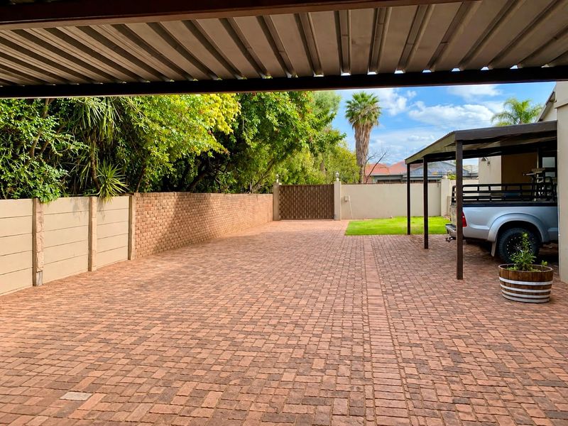 Spacious paved driveway featuring a covered carport, secure perimeter brick walling, and a gated entrance with a well-maintained lawn area.