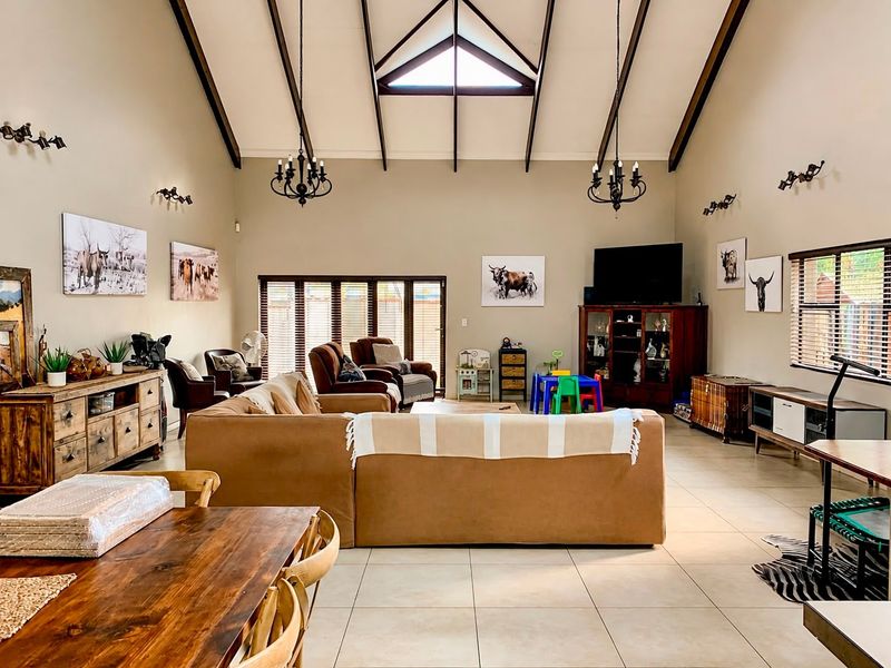 Spacious open-plan living area featuring a high vaulted ceiling with exposed timber beams, tiled flooring, and abundant natural light from a clerestory window.