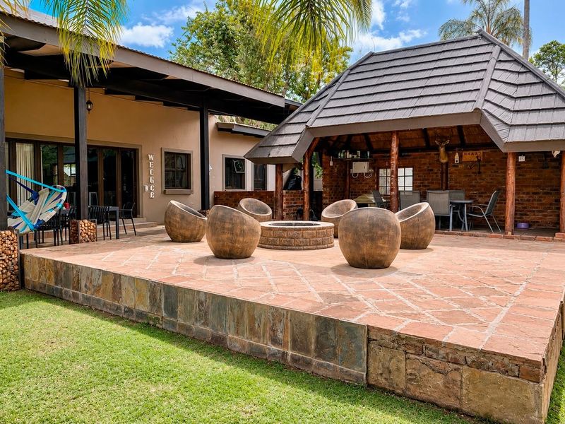 Spacious outdoor entertainment area featuring a raised stone patio, a covered veranda, and a charming thatched-roof gazebo with a built-in fire pit.