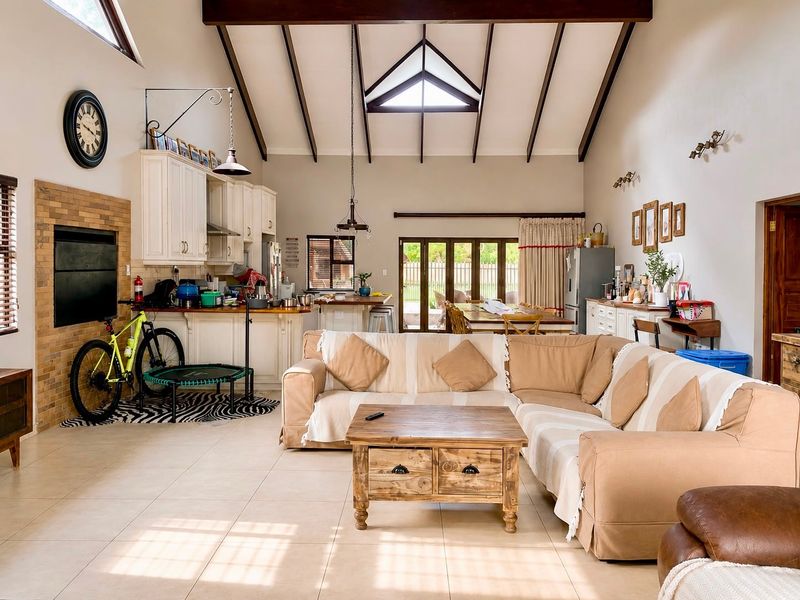 Spacious open-plan living and kitchen area featuring a high vaulted ceiling with exposed beams, a brick fireplace, and direct access to the outdoor patio.