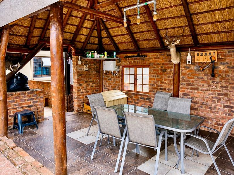 Covered outdoor patio featuring a rustic thatched roof, exposed brick walls, tiled flooring, and a built-in brick braai area, ideal for outdoor entertaining.