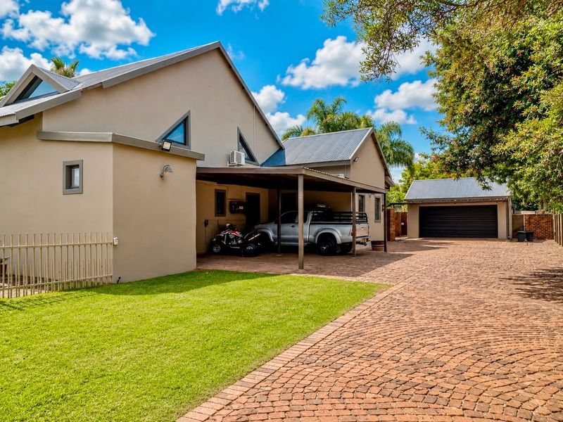 A well-maintained residential property featuring a paved driveway, a covered carport, and a separate detached garage with a metal roof.