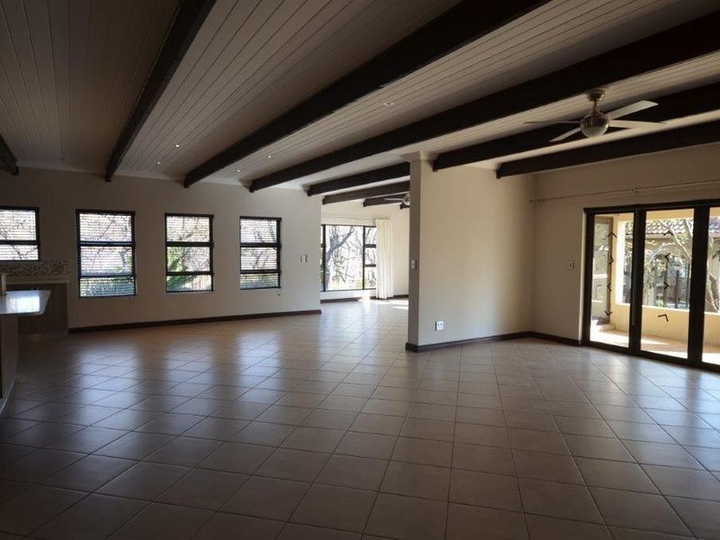 Spacious open-plan living area featuring exposed timber beams, tiled flooring, and large windows providing ample natural light with direct access to the patio.