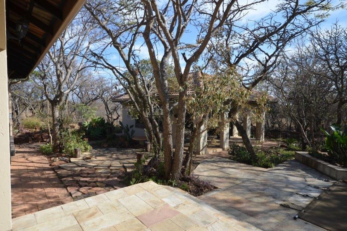 A spacious rear garden area featuring stone paving, a covered outdoor structure, and mature trees, providing a natural and tranquil outdoor living space.