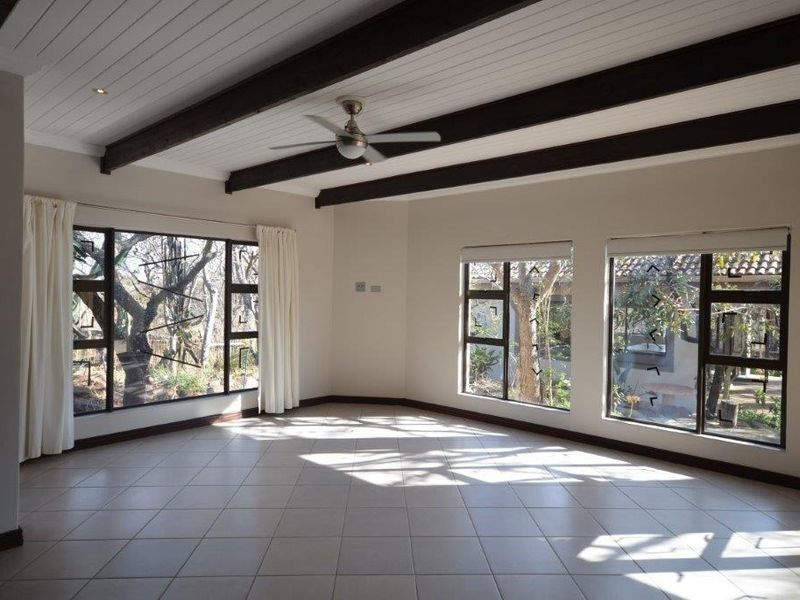 Spacious, light-filled living area featuring exposed timber ceiling beams, tiled flooring, and large windows overlooking the garden.