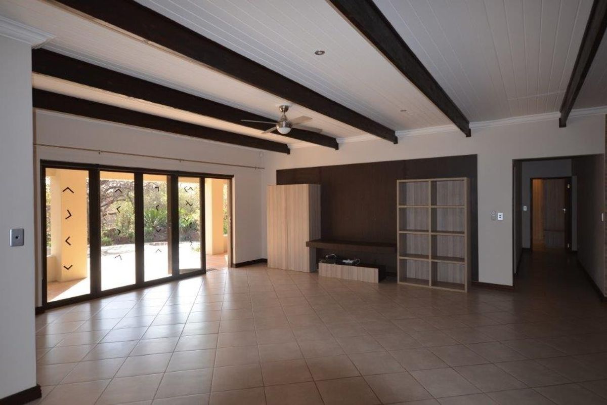 Spacious living area featuring exposed timber ceiling beams, tiled flooring, and large sliding glass doors providing access to the outdoor patio.