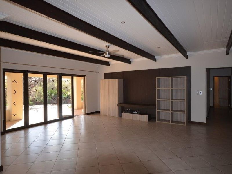 Spacious living area featuring exposed timber ceiling beams, tiled flooring, and large sliding glass doors providing access to the outdoor patio.