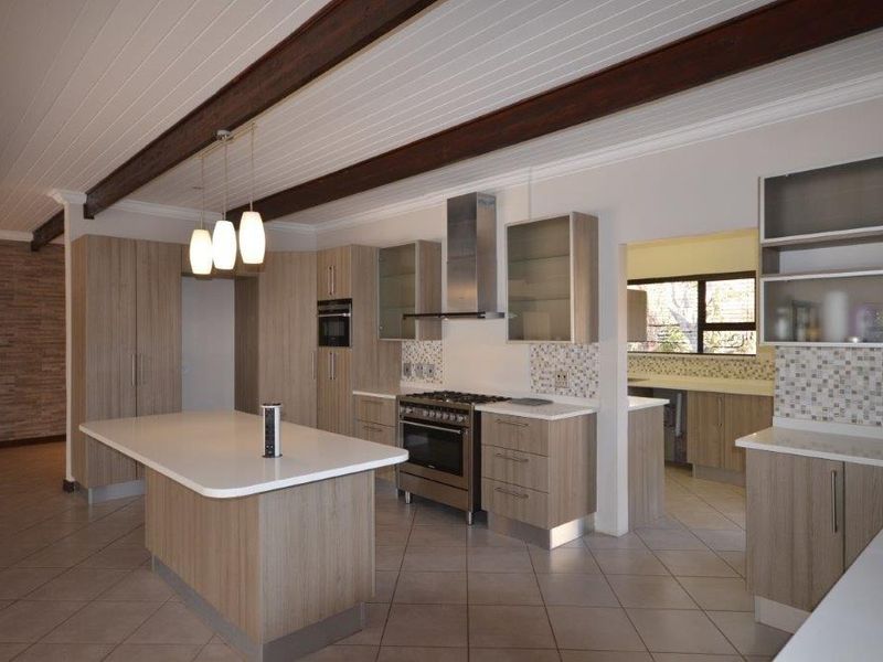 Modern kitchen featuring a central island, stone countertops, built-in stainless steel appliances, and timber ceiling beams, offering a clean and functional workspace.