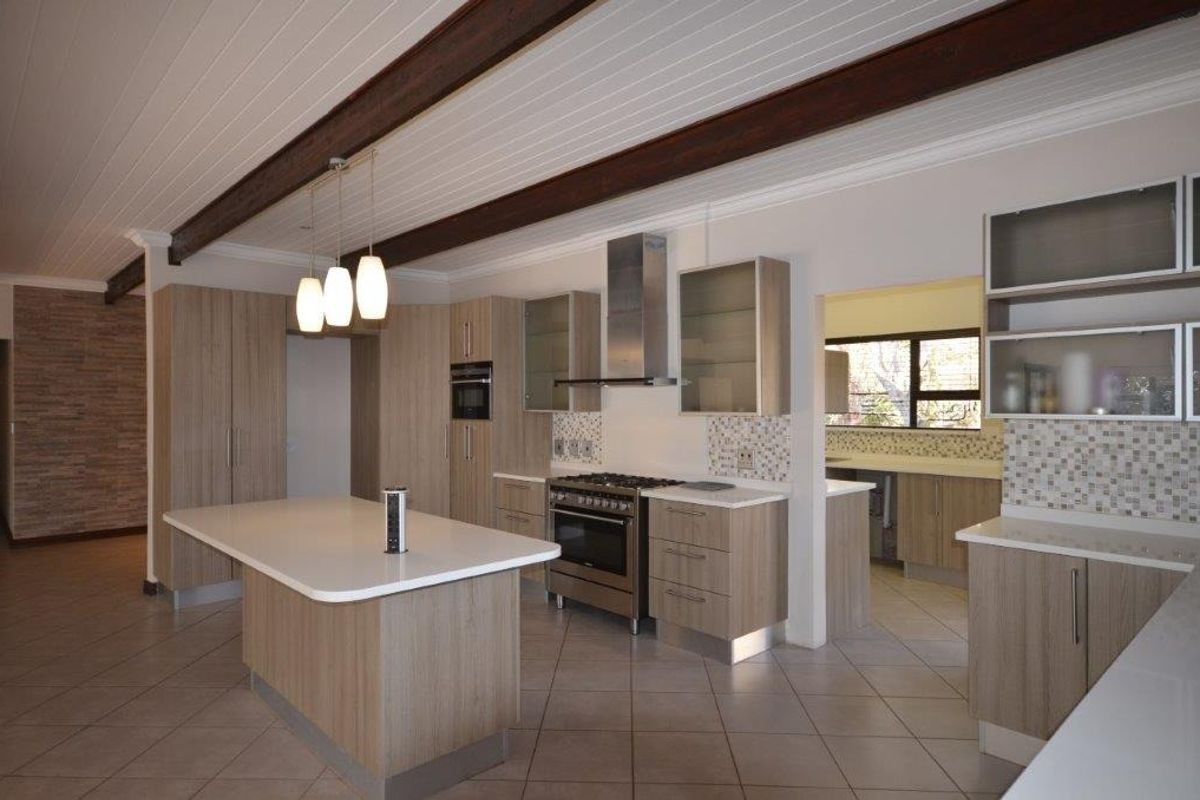 Modern kitchen featuring a central island, stone countertops, built-in stainless steel appliances, and timber ceiling beams, offering a clean and functional workspace.