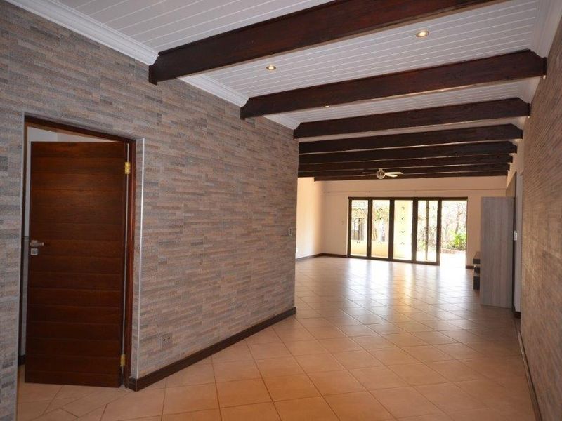 Spacious living area featuring exposed timber ceiling beams, stone-clad feature walls, tiled flooring, and large sliding glass doors leading to the exterior.