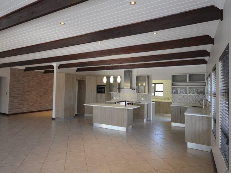 Spacious open-plan kitchen and living area featuring exposed timber beams, a central island, modern cabinetry, and a decorative stone feature wall.