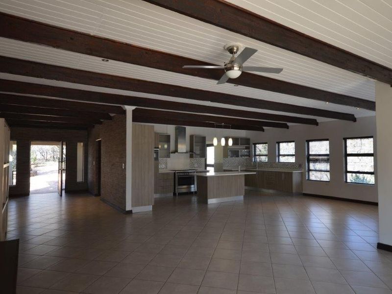 Spacious open-plan kitchen and living area featuring exposed timber ceiling beams, tiled flooring, and a modern kitchen island with built-in cabinetry.