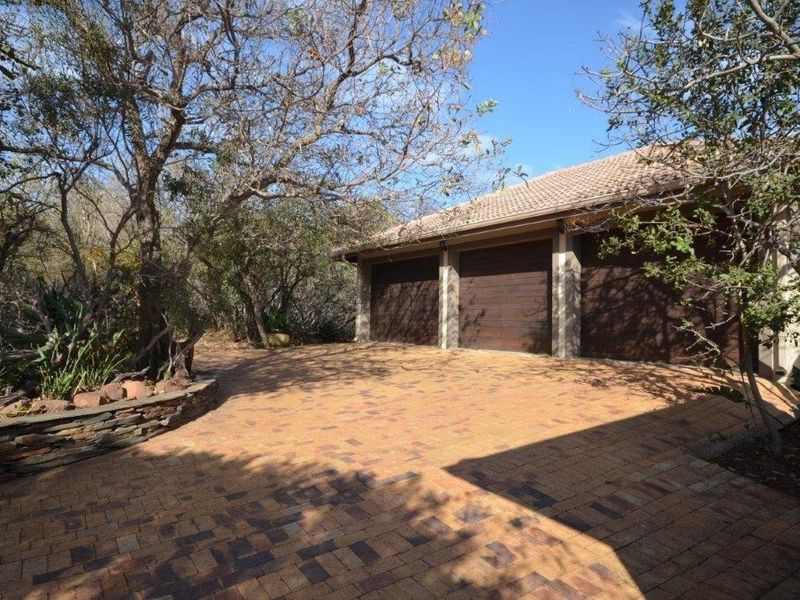 A triple garage with wooden doors and a paved driveway, set within a landscaped garden area with a stone retaining wall.