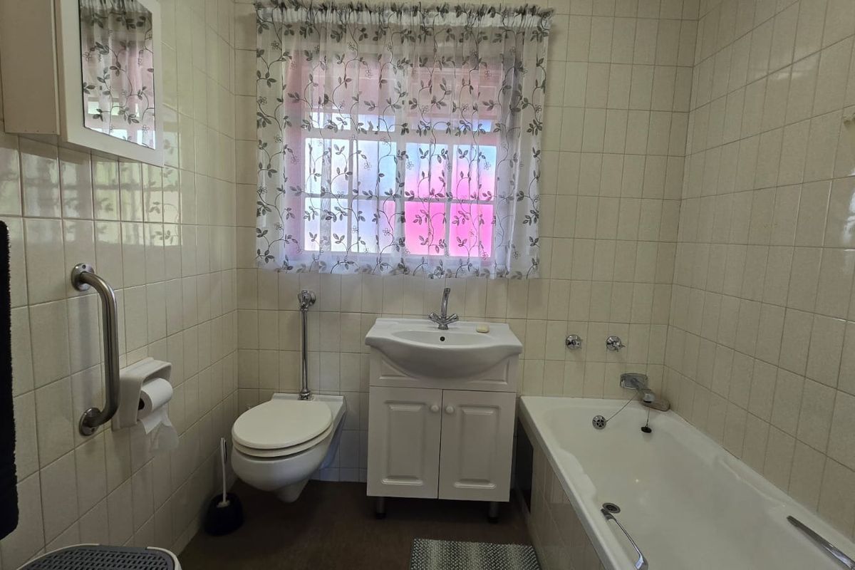 A functional bathroom featuring a wall-mounted toilet, vanity basin, and bathtub with tiled walls and a safety grab rail.