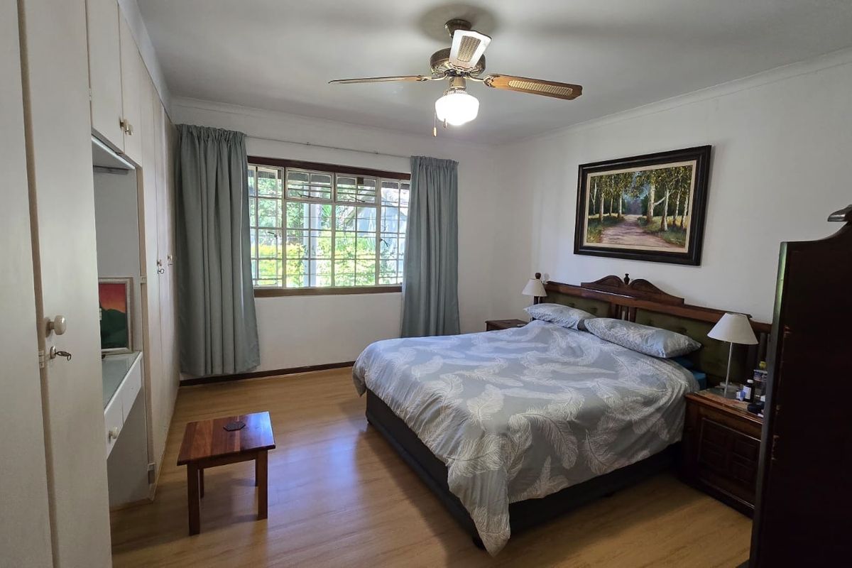 A well-maintained bedroom featuring laminate flooring, built-in cupboards, and a ceiling fan, offering a comfortable and functional living space.