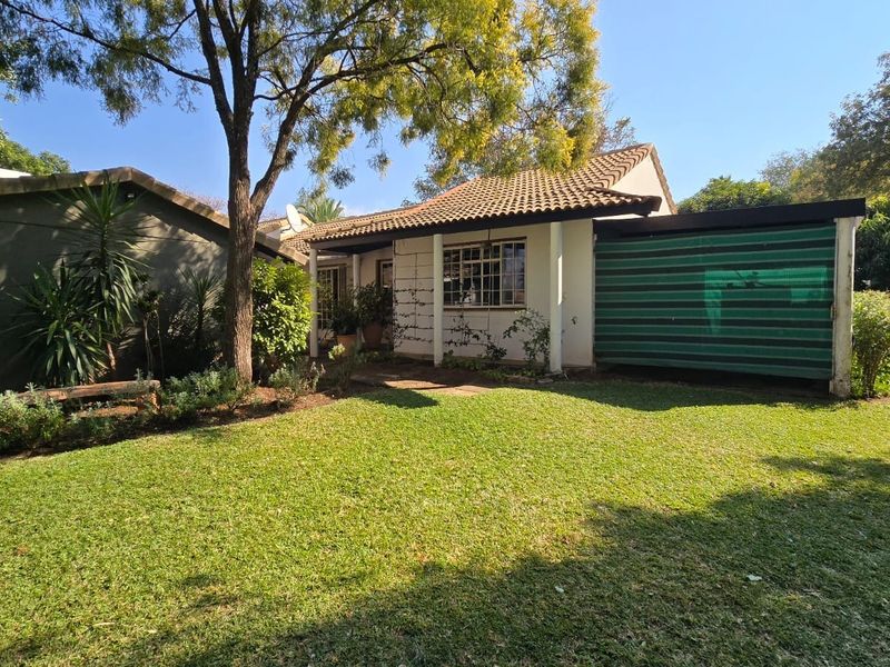 A view of the rear exterior of the retirement unit, featuring a tiled roof, covered patio area, and a well-maintained garden.
