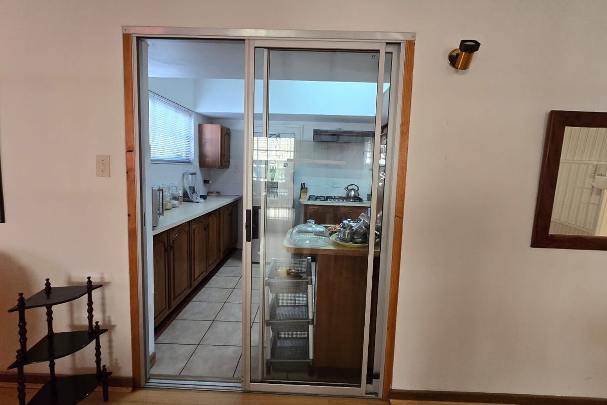 A view through a sliding glass door into a functional kitchen featuring wooden cabinetry, tiled floors, and a gas hob with an extractor fan.