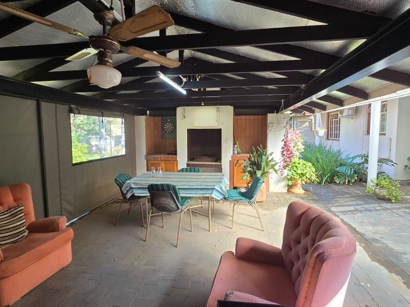 Spacious covered patio featuring a built-in braai, exposed timber beam ceiling, and durable paved flooring, ideal for outdoor entertaining and relaxation.