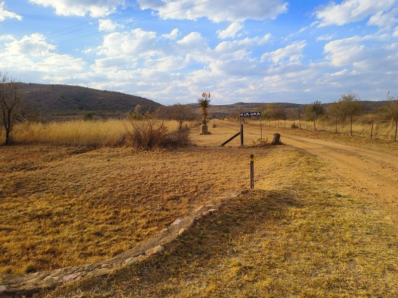 A view of the entrance to the vacant residential land, featuring a dirt road, wire fencing, and natural landscape.