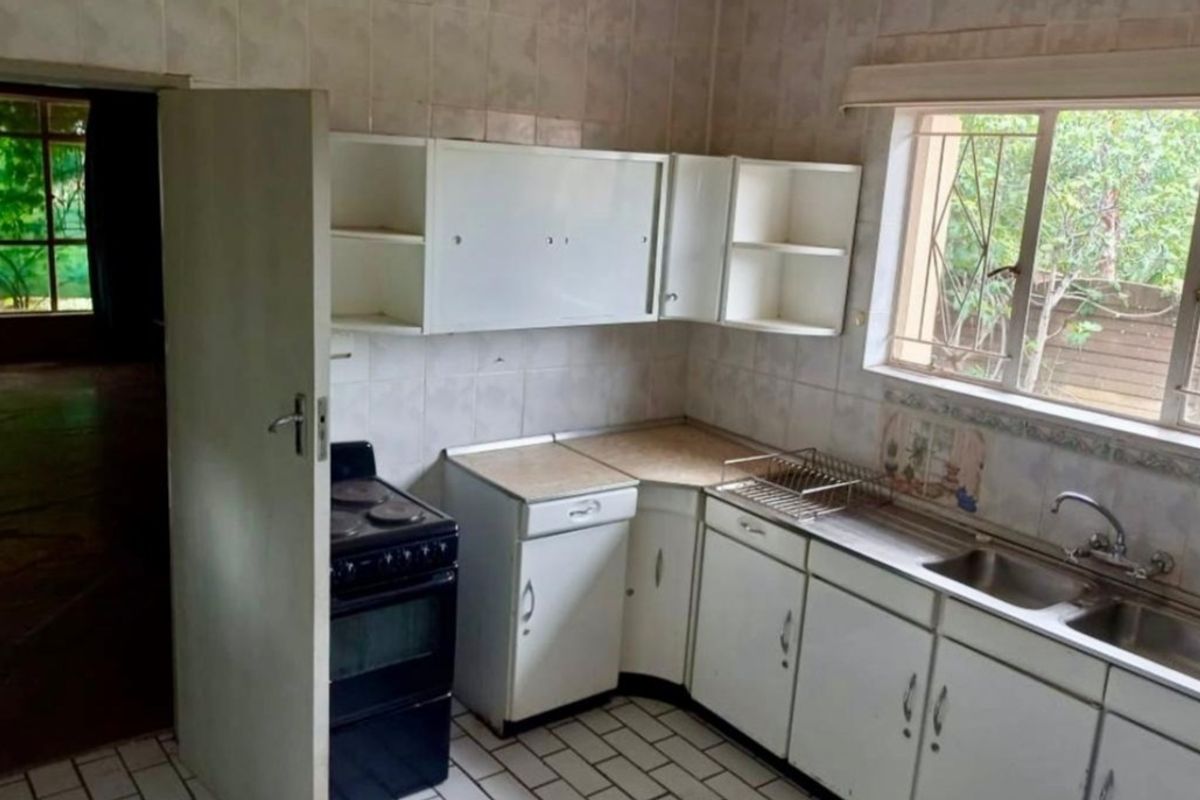 A functional kitchen featuring original cabinetry, tiled splashbacks, and a stainless steel sink, offering potential for a modern renovation.