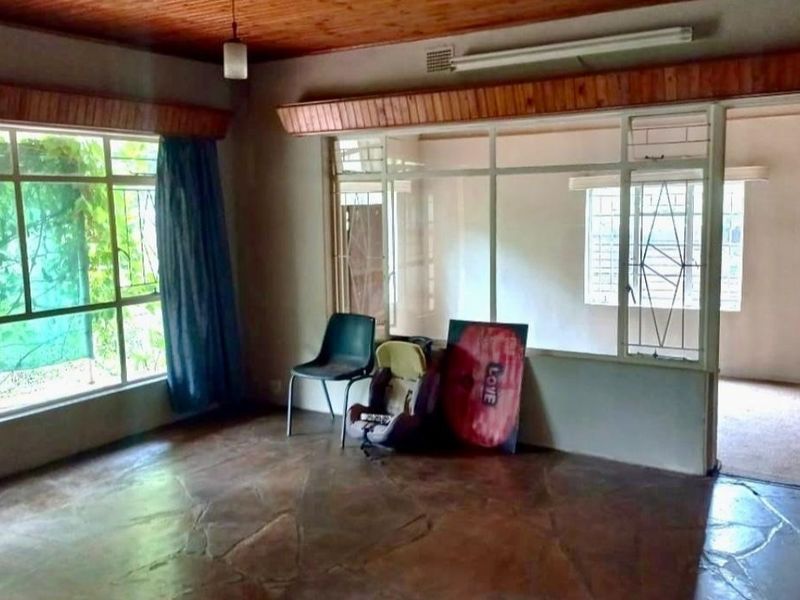 Spacious living area featuring natural stone flooring, a wooden ceiling, and an internal glass partition, offering a dated but functional layout.