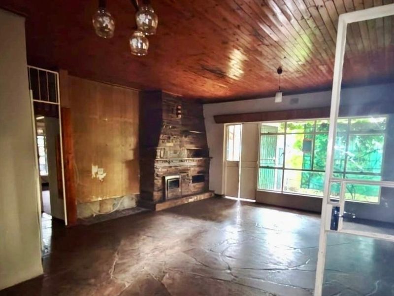 Spacious living room featuring a prominent stone fireplace with a built-in stove, timber-clad ceiling, and flagstone flooring, offering a rustic foundation for renovation.