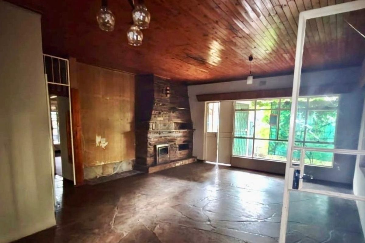 Spacious living room featuring a prominent stone fireplace with a built-in stove, timber-clad ceiling, and flagstone flooring, offering a rustic foundation for renovation.