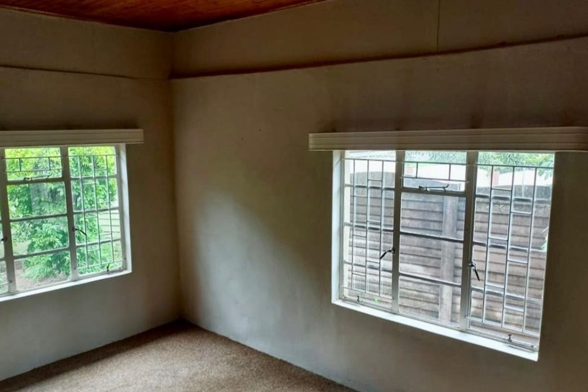 An empty bedroom featuring timber ceilings, carpeted flooring, and steel-framed windows with security burglar bars.