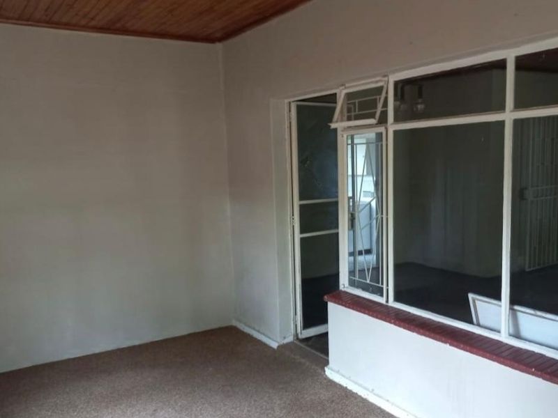 An enclosed patio area featuring a timber ceiling, large glass windows, and a security gate, offering a blank canvas for renovation.