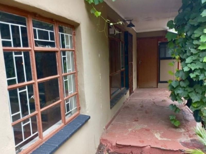 A covered outdoor patio area featuring timber-framed windows with security bars, requiring some maintenance and cosmetic updates to the flooring and wall finishes.