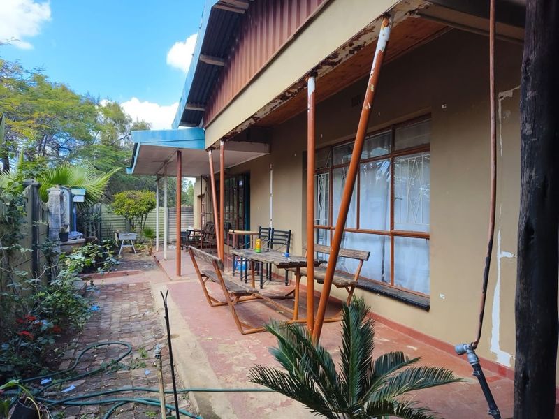A covered outdoor patio area featuring paved flooring and metal support columns, showing signs of wear and requiring maintenance.