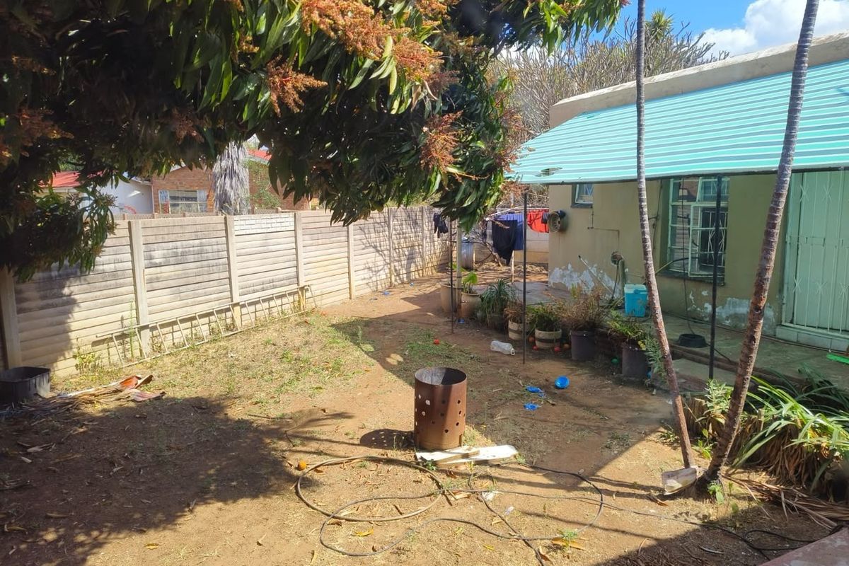 Rear garden area featuring a precast concrete boundary wall, metal roof awning, and exterior wall surfaces requiring maintenance and landscaping.