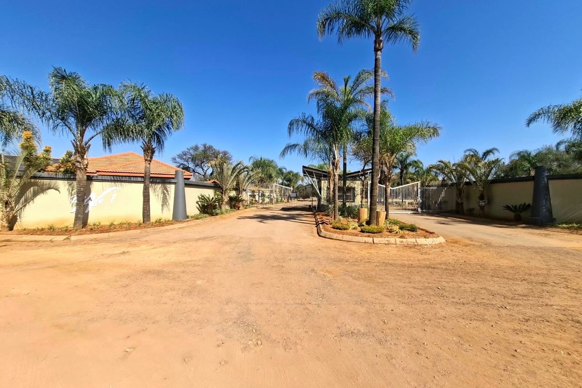 Entrance view of a residential estate featuring a secure gated access point, perimeter walling, and established palm tree landscaping.