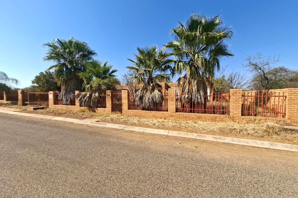 Street view of a residential property featuring a brick boundary wall with integrated metal fencing and mature palm trees.