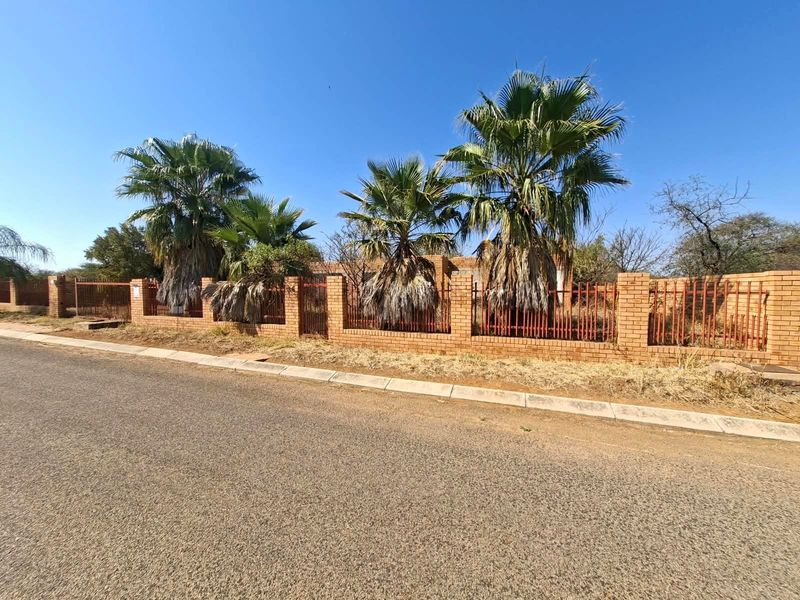 Street view of a residential property featuring a brick boundary wall with integrated metal fencing and mature palm trees.