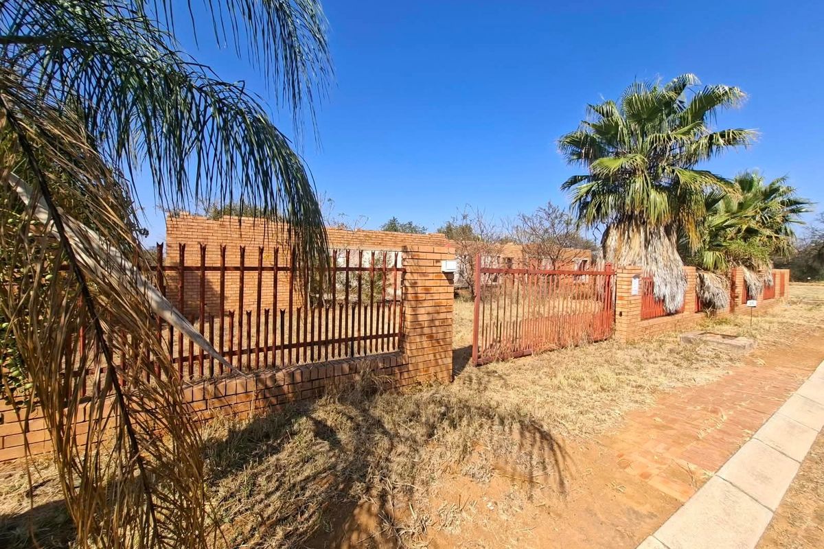 Street view of a residential property featuring a brick boundary wall, metal security fencing, and overgrown landscaping.