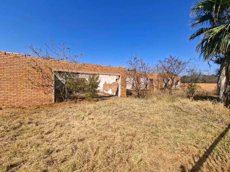 A view of a dilapidated brick structure on a vacant residential lot, showing significant structural damage and overgrown grounds.
