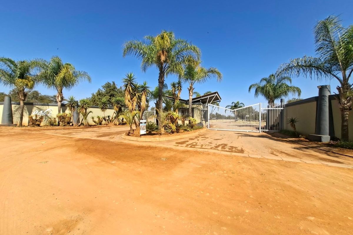 Front entrance view of a residential estate featuring a secure gated access point, perimeter walling, and established palm trees.