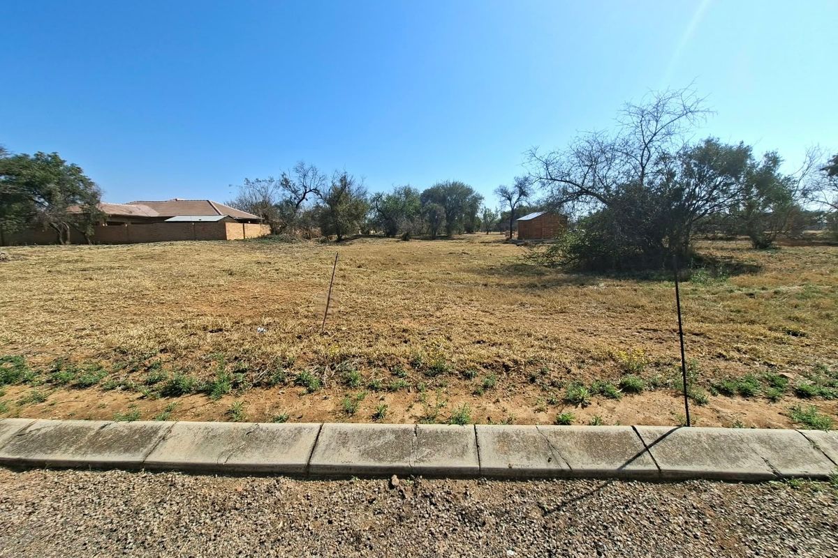A vacant residential plot featuring a concrete curb, level terrain, and established trees, offering a clear space for future development.