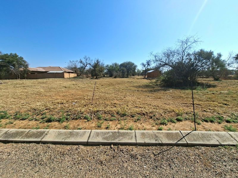 A vacant residential plot featuring a concrete curb, level terrain, and established trees, offering a clear space for future development.